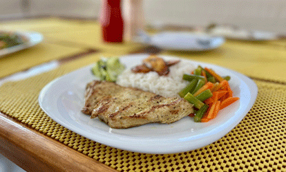 Um prato de arroz com frango grelhado e legumes cozidos, servido com banana-da-terra frita.