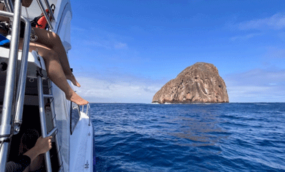 Ilhéu visto de um barco com vários turistas.